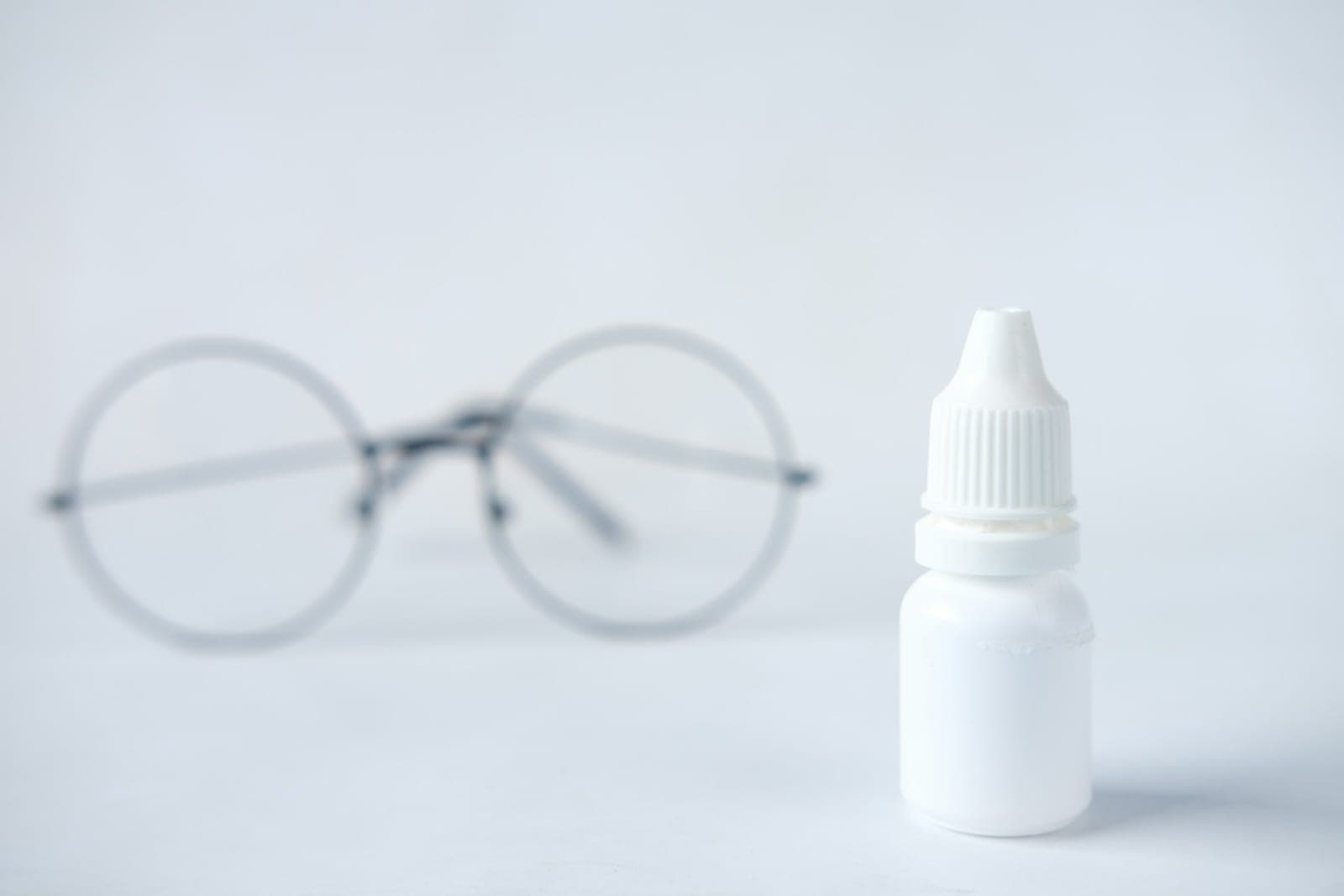 Eine Brille und eine Tropfflasche auf hellem Hintergrund