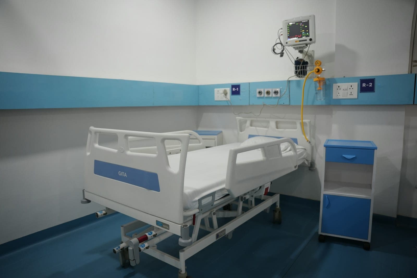 Une chambre de patient vide avec un lit réglable et un moniteur fixé au mur