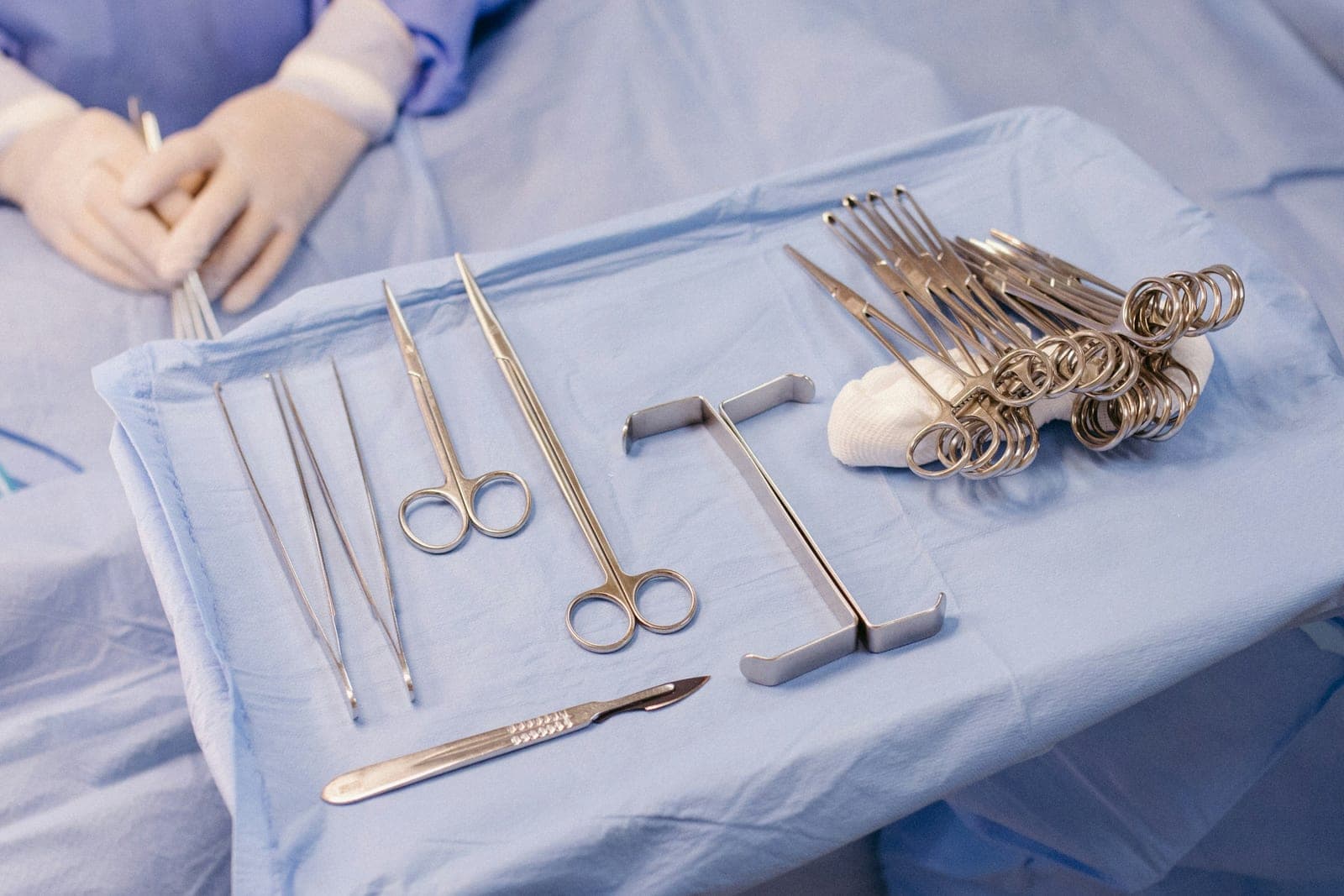 Chirurgische Instrumente auf einem blauen sterilen Tuch, dazu Hände in Handschuhen